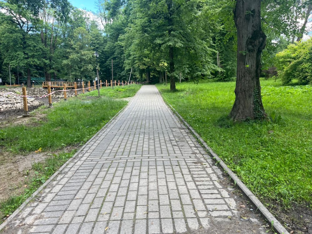 Jasna, równa alejka z kostki; po lewej teren robót ogrodzony palikami.
