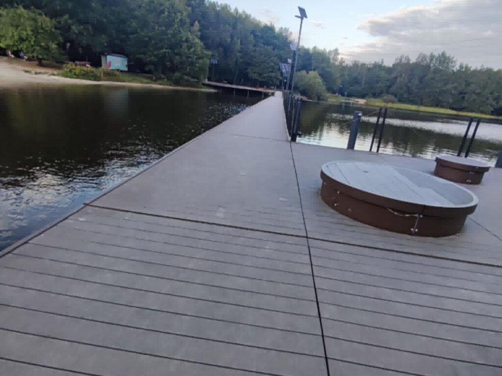 Szeroki pomost z desek kompozytowych nad wodą w Stargańcu, okrągłe siedziska i latarnie.