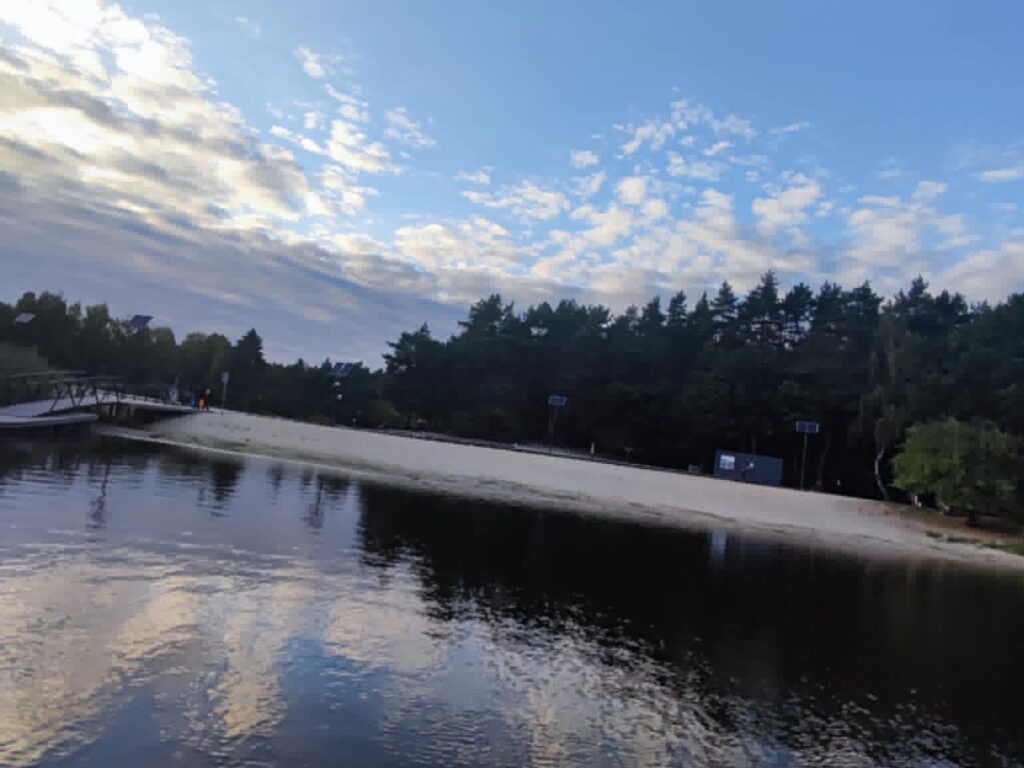 Tafla zbiornika o zmierzchu, w tle kładka nad wodą i ściana lasu.