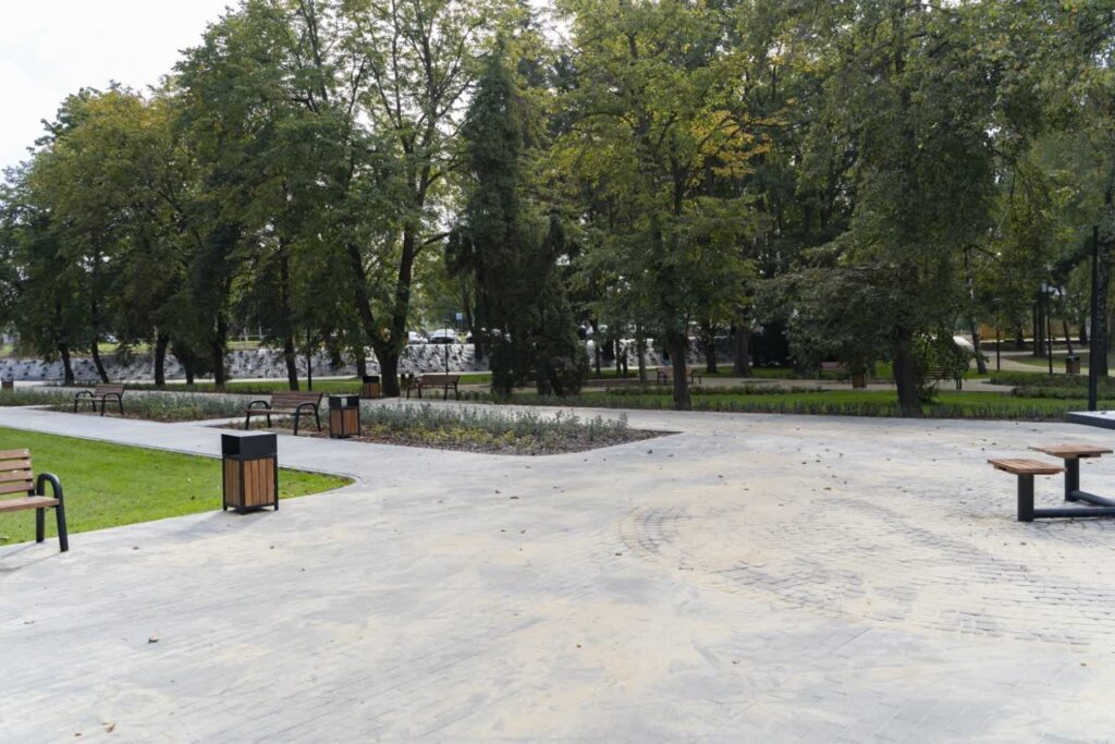 Plac z kostki betonowej, pośrodku drobniejsza kostka ułożona w koła, z placu rozchodzą się alejki.