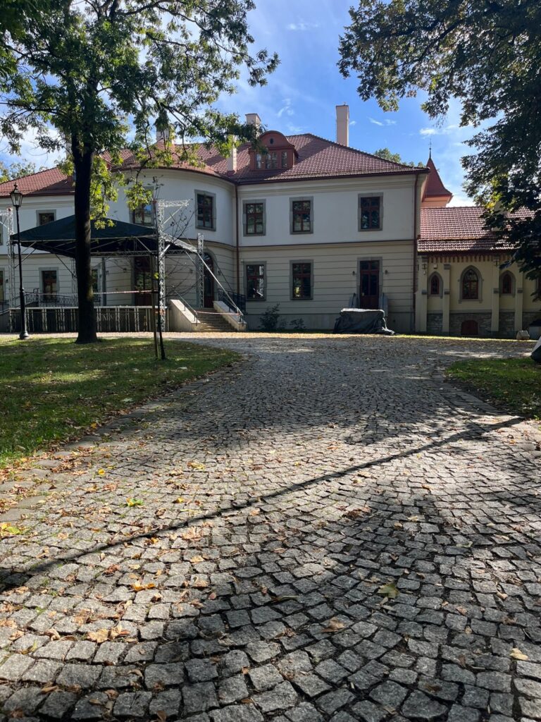 Plac z kostki granitowej przy pałacu, do drzwi prowadzą schody, obok stalowa konstrukcja sceny.