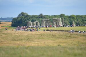 Krąg kamieni Stonehenge, a przed nim zwiedzający idący ścieżką przez płaską, trawiastą równinę
